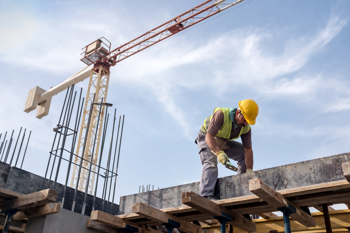 Construction worker sawing on site with crane in background
